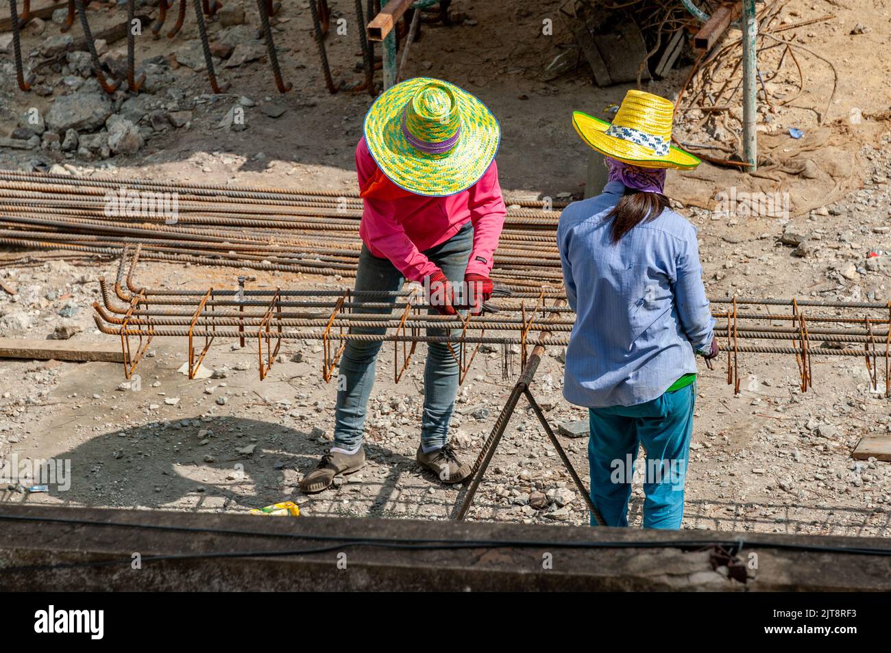 Zwei Bauarbeiter verteilen gleichmäßig geschlossene Stahlstäbe entlang der Länge der verformten Stäbe und binden sie mit Stahldrähten zusammen. Stockfoto