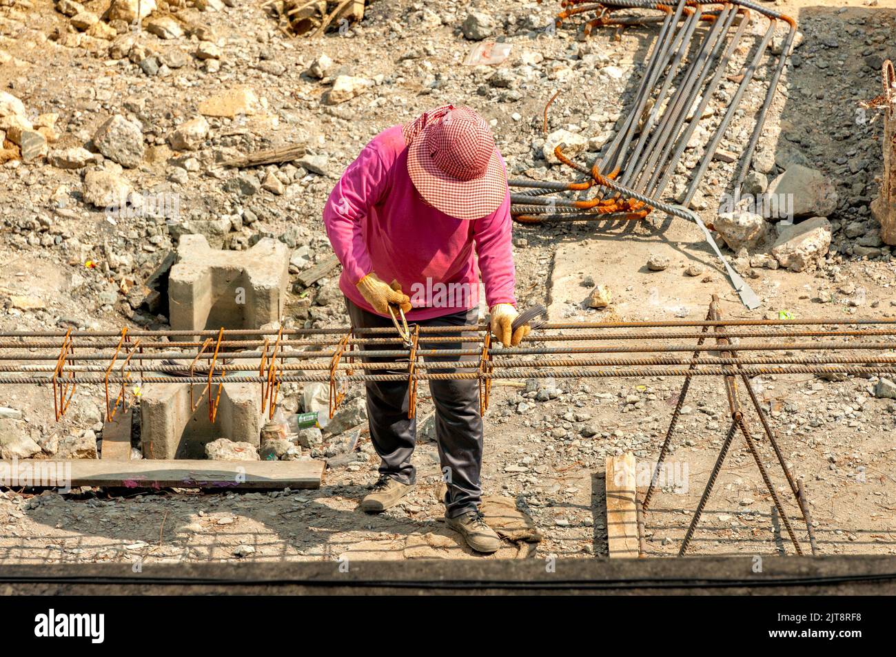 Ein Bauarbeiter verteilt ebenfalls geschlossene Stahlstäbe entlang der Länge der verformten Stäbe und bindet sie mit Stahldrähten zusammen. Stockfoto