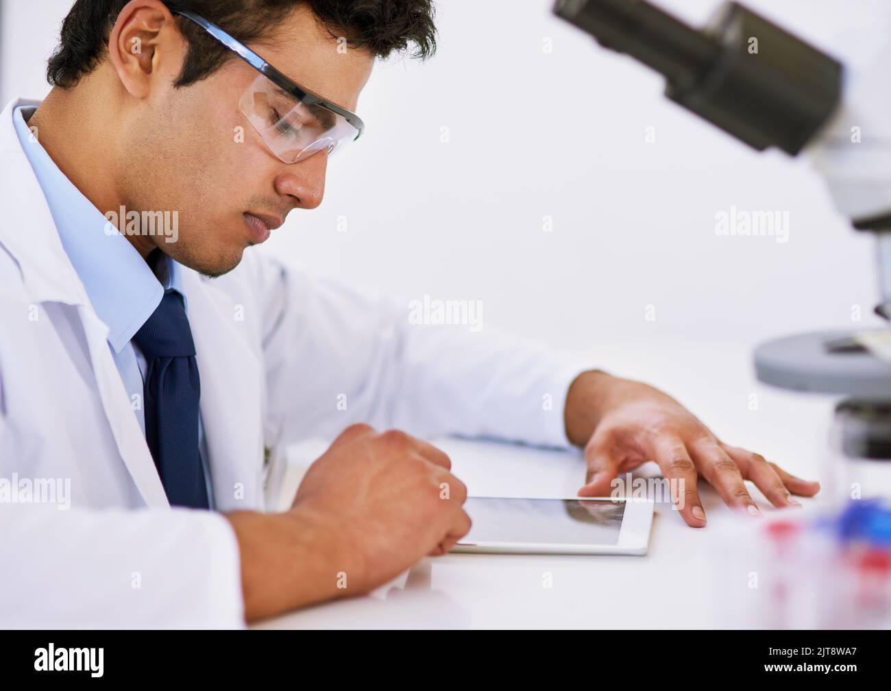 Sorgfältig aufzeichnen seiner Ergebnisse. Ein Labortechniker mit einem digitalen Tablet und Mikroskop, während er in einem Labor sitzt. Stockfoto