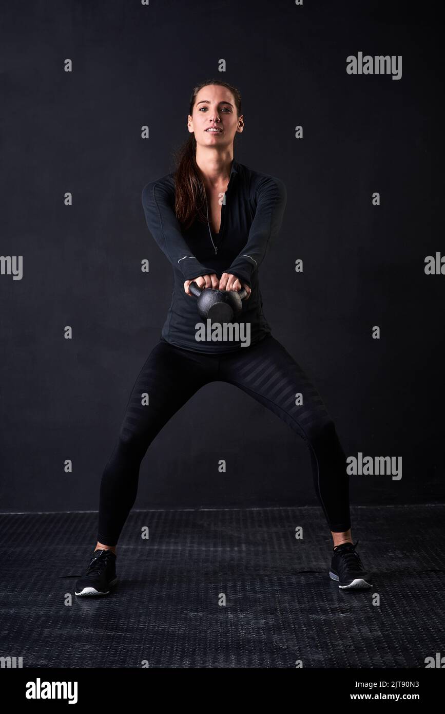 Mit jedem Lift fitter und stärker werden. Studioporträt einer jungen Frau in Turnkleidung, die mit einer Kugelhantel vor dunklem Hintergrund arbeitet. Stockfoto