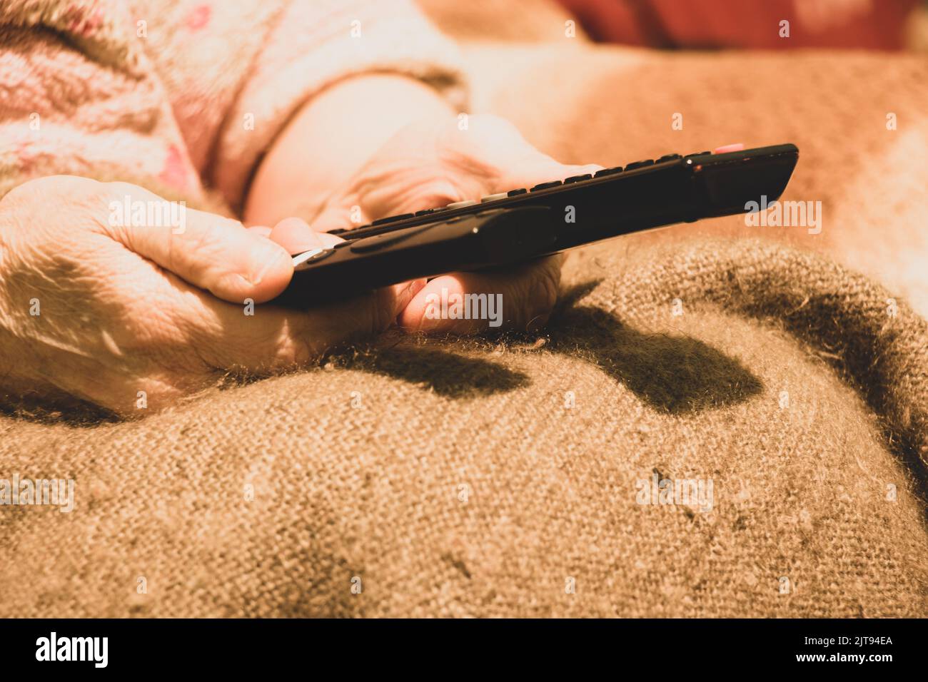 Eine alte Frau hält zu Hause zwei Fernbedienungen vom Fernseher in der Hand und schaut sich einen Film an, die Fernbedienung liegt in der Hand der Frauen Stockfoto