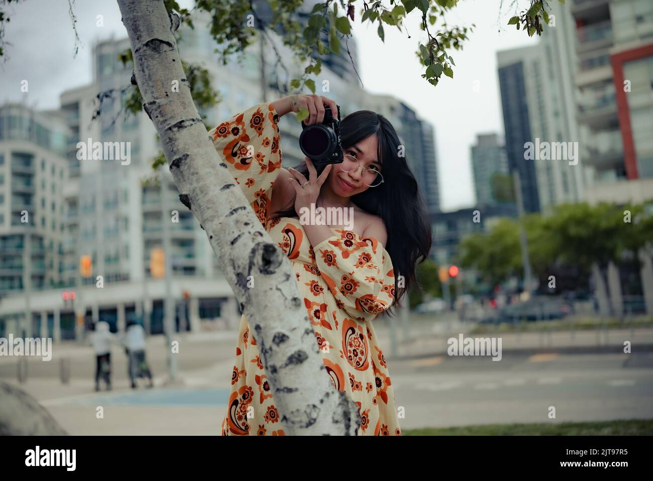 Eine vertikale Aufnahme einer asiatischen Frau in einem Kleid, die die Kamera hält und die Kamera in der Straße von Toronto anschaut Stockfoto