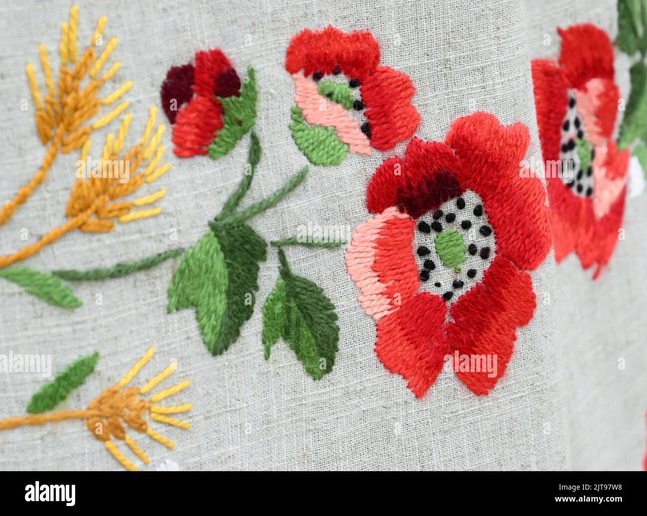 Nahaufnahme traditionelle Stickerei von Mohnblumen und Weizenspikelets auf grauem Leinentuch Stockfoto