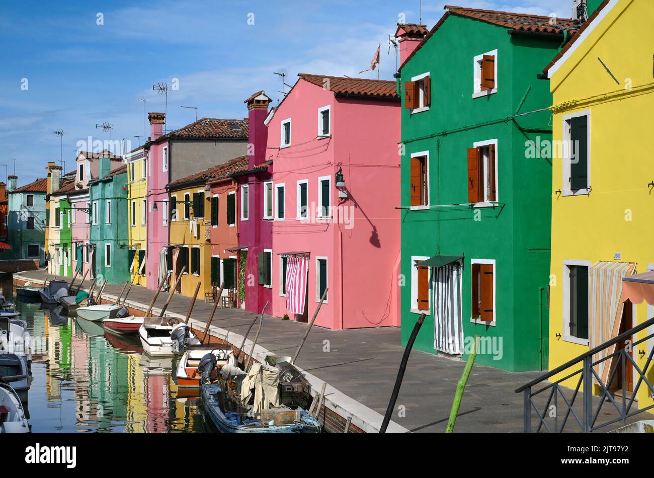 Boote, die an sonnigen Tagen in der Nähe von bunten Häusern auf ruhigem Kanalwasser vor blauem Himmel auf der Straße der Insel Burano in Italien schwimmen Stockfoto