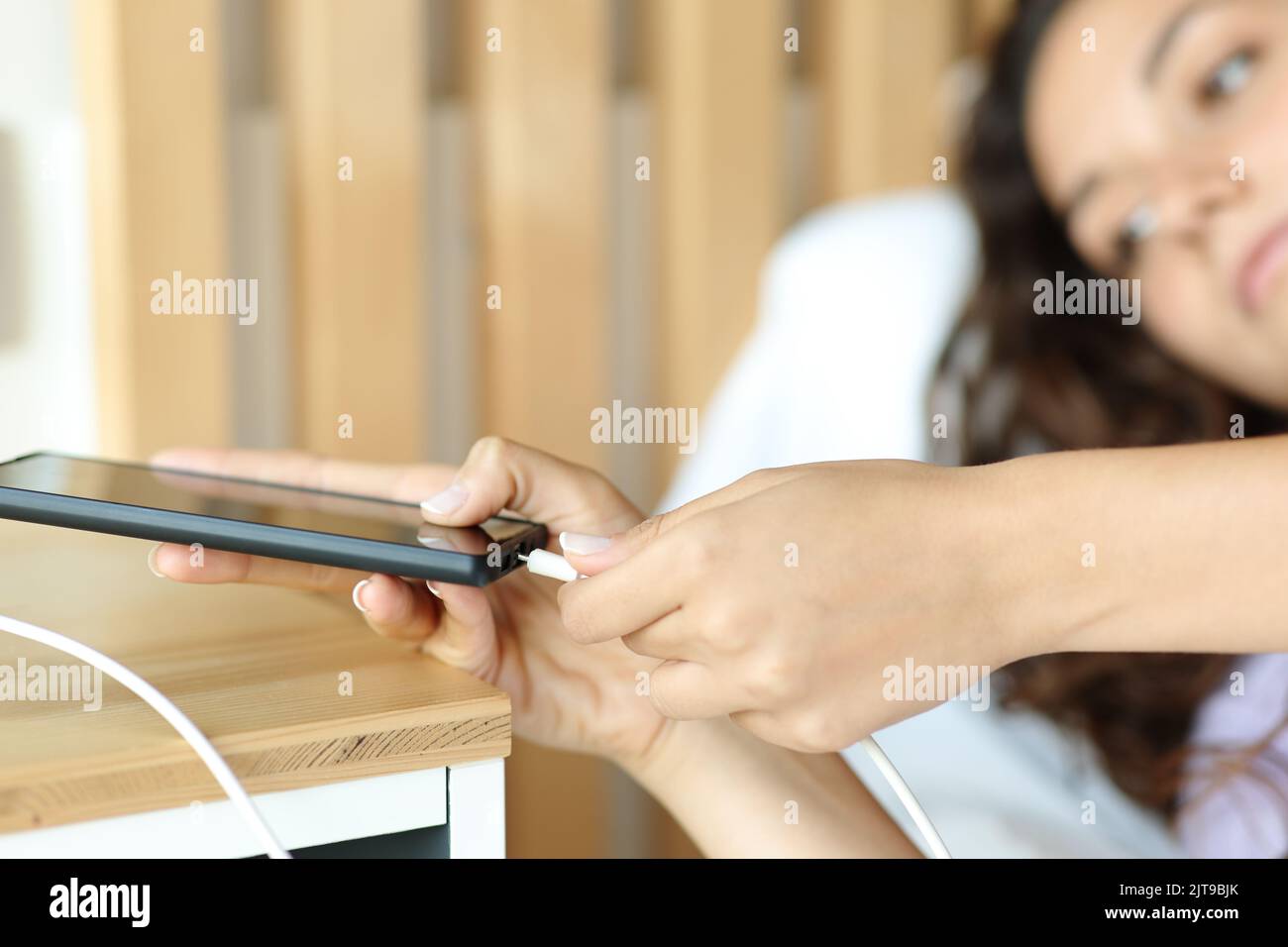 Nahaufnahme einer Frau, die ein usb-Ladegerät auf einem Smartphone in einem Schlafzimmer anschließt Stockfoto