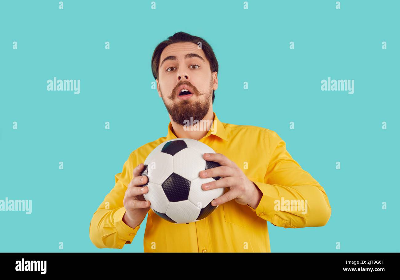 Studioaufnahme eines lustigen schüchternen Mannes im Hemd, der den Fußball mit einem verängstigten Gesichtsausdruck hält Stockfoto