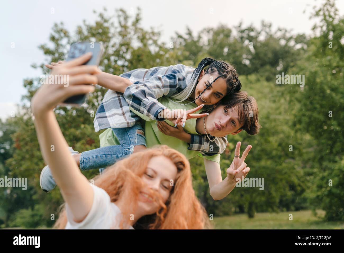 Ginger schönes Mädchen mit Smartphone nehmen verrückte Selfie im Freien, mit ihren zwei Freunden machen Gesichter. Technologie der neuen Generation. Lifestyle in der Stadt. Stockfoto