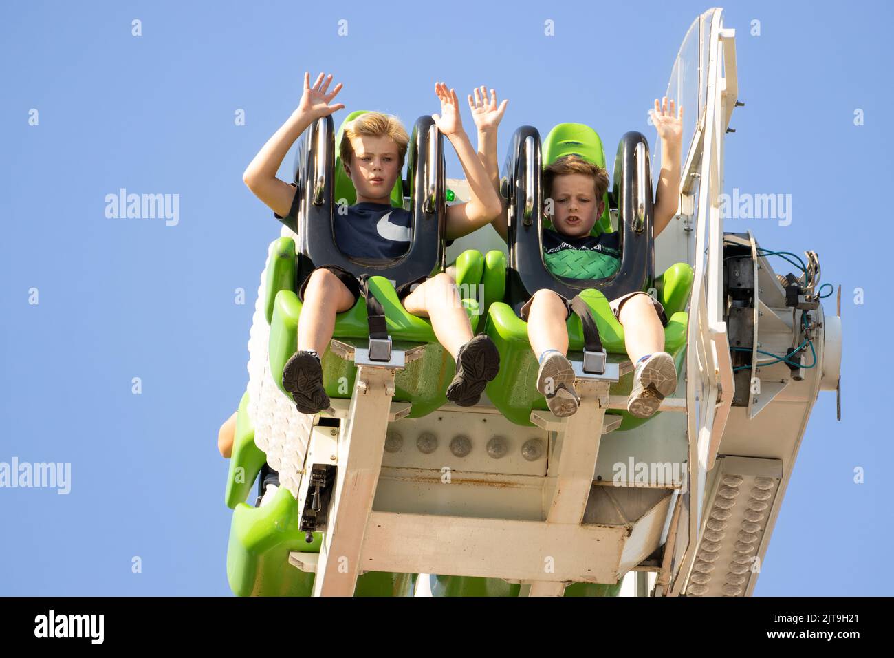 Zwei Kinder merken, dass sie auf dem Jahrmarkt bei einer „Booster“-Pendelfahrt herunterfallen werden. Stockfoto