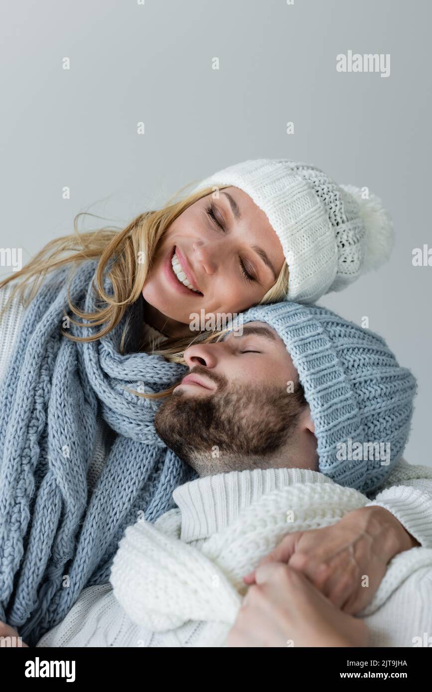 Happy blonde Frau in gestrickten Schal umarmt mit bärtigen Freund im Winter Hut isoliert auf grau, Stock Bild Stockfoto