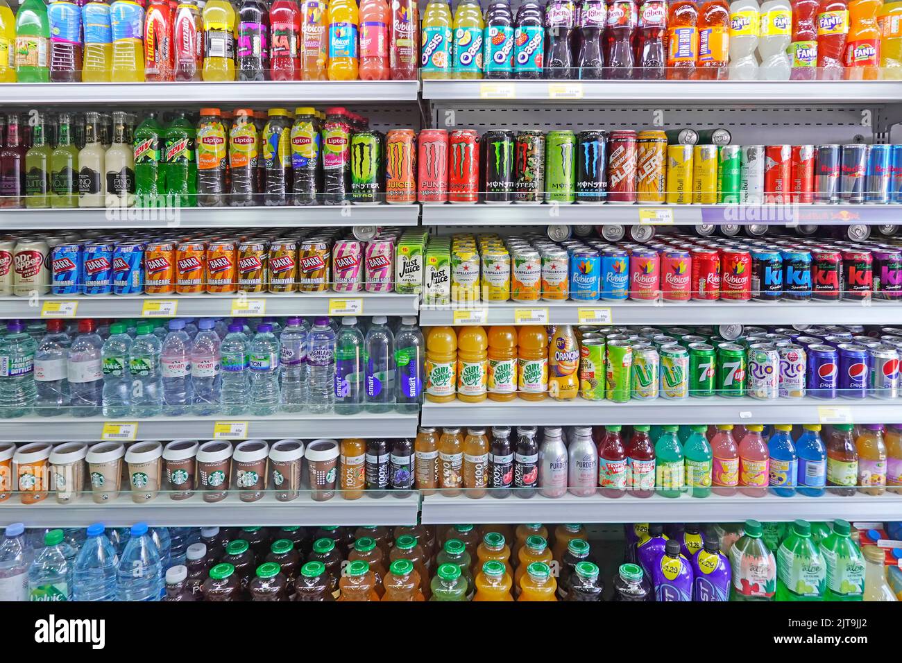 Reihen von bunten Softdrink-Dosen und -Flaschen einige zuckerhaltige, hohe Zuckergehalte und CO2 kohlensäurehaltige Getränke auf Regalen im Convenience-Shop Essex England UK Stockfoto