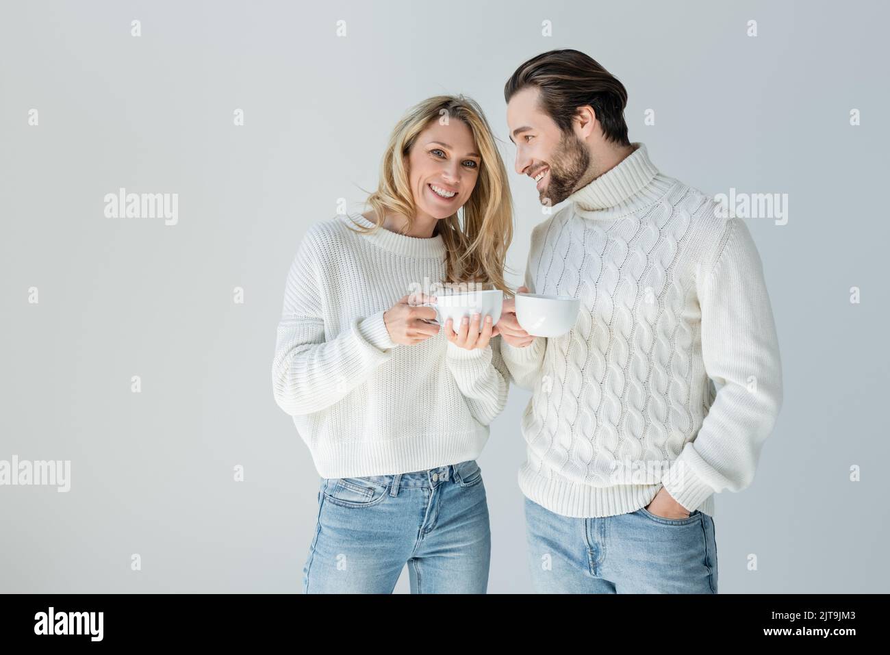 Glücklicher Mann und fröhliche Frau in weißen Strickpullover mit Tassen Kaffee isoliert auf grau, Stock Bild Stockfoto
