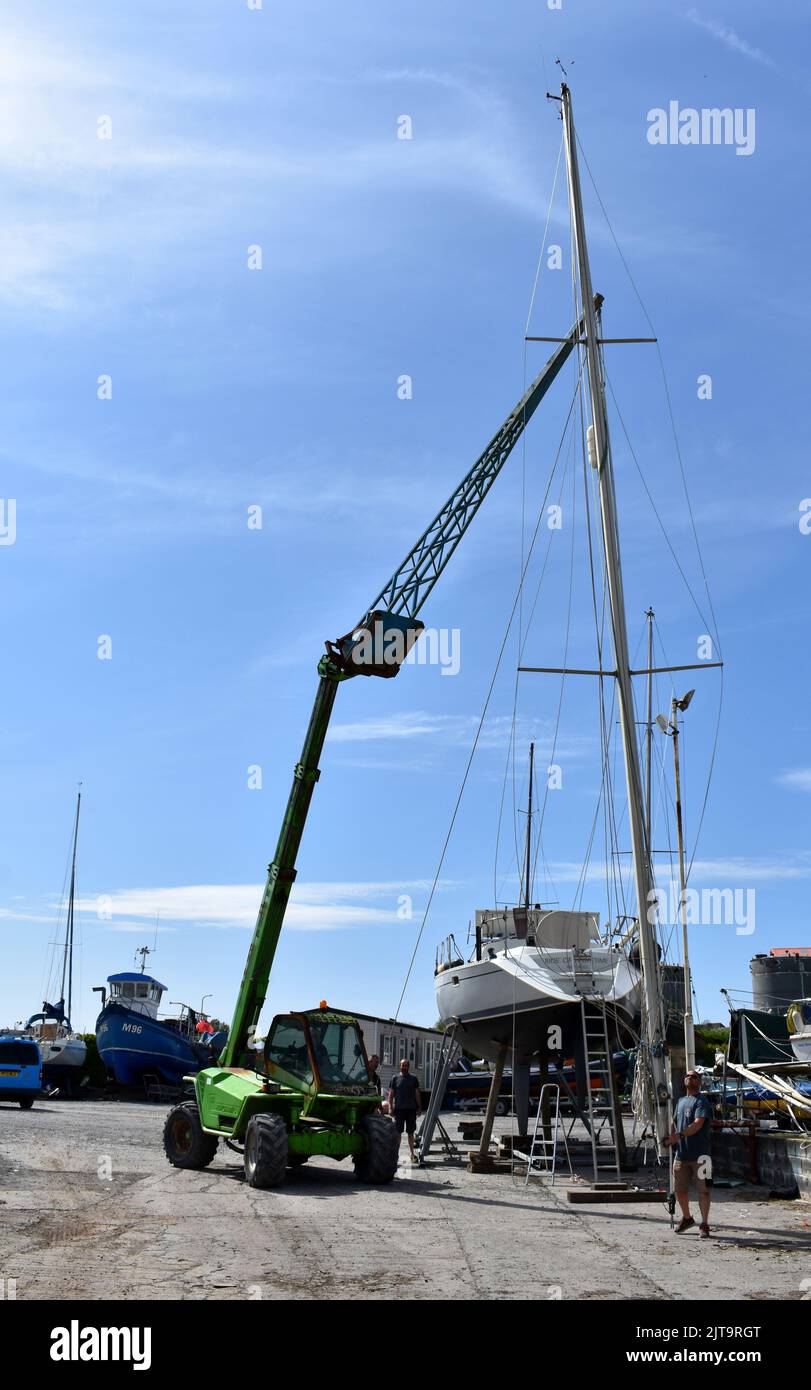 Kran, der einen Mast wieder auf ein Segelboot in East Llanion boatyard, East Llanion, Pembrokeshire, Wales, hebt Stockfoto