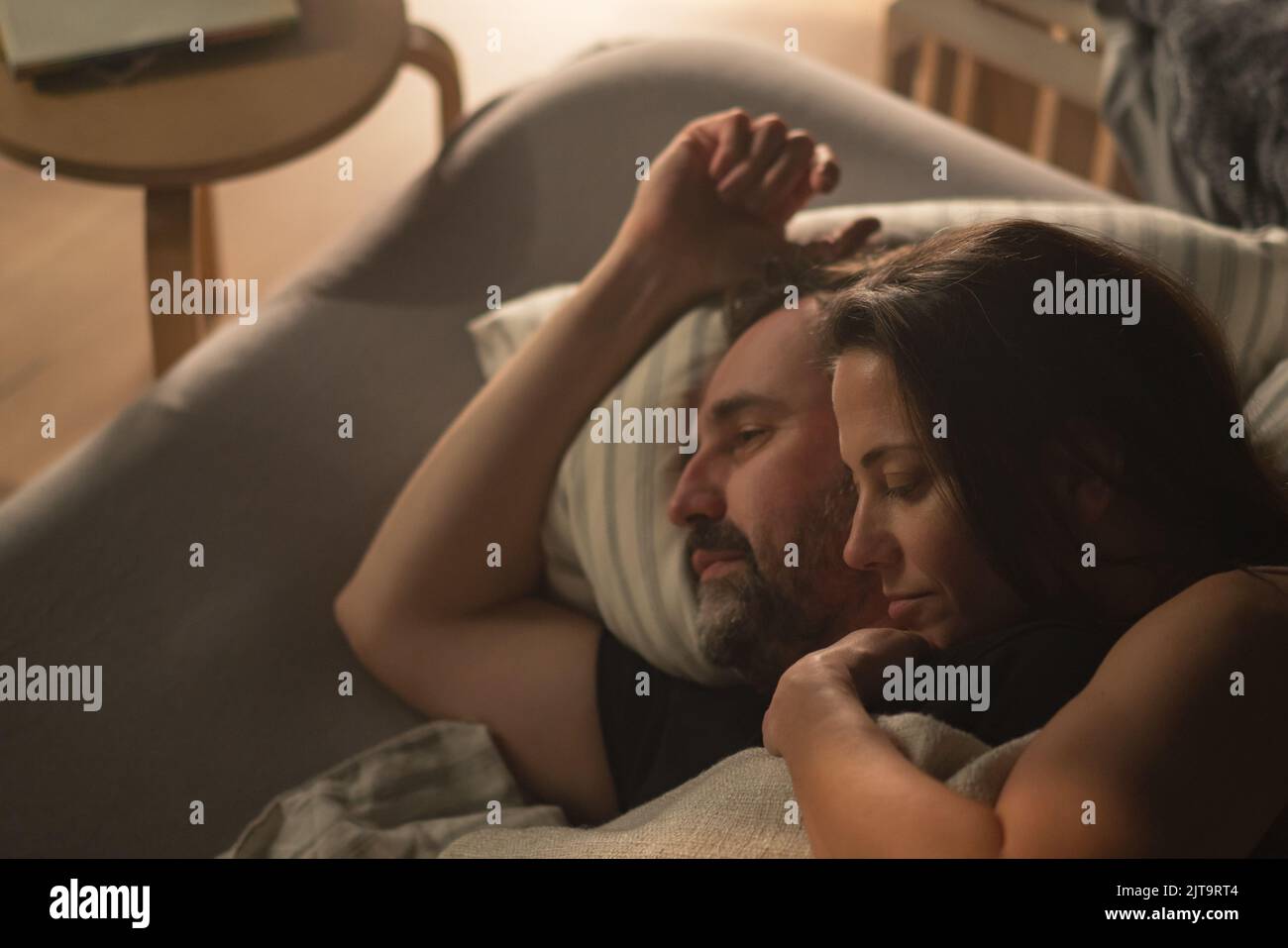 Ein Paar mit mittleren Erwachsenen liegt nachts im Bett und umarmt das Konzept der Intimität. Stockfoto