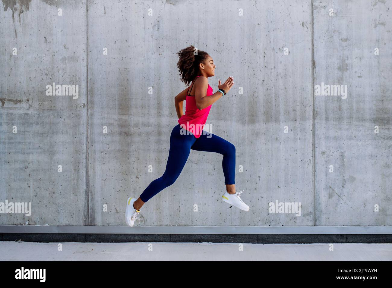 Junge multirassische Mädchen joggen und springen in der Stadt, vor der Betonwand, Seitenansicht. Stockfoto