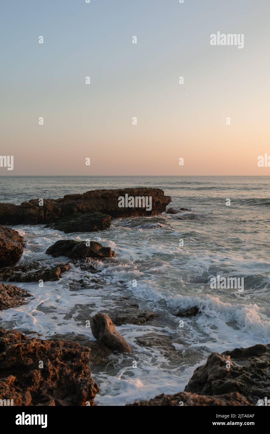 Eine vertikale Aufnahme der malerischen Sonnenuntergangsszene über Felsen im Atlantik in Portugal Stockfoto