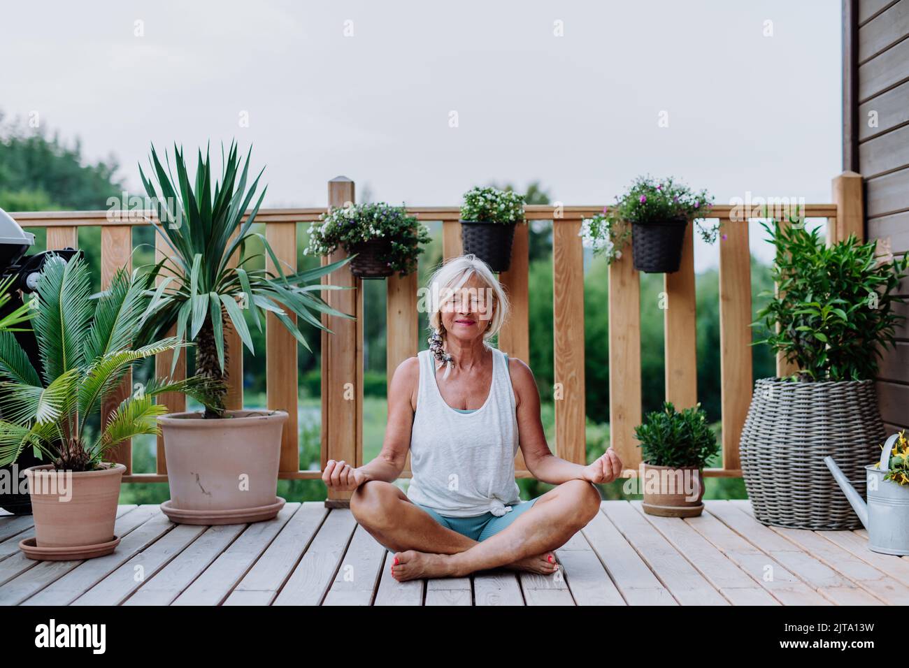 Eine ältere Frau, die im Sommer draußen auf einer Terrasse sitzt und Yoga-Übungen macht. Stockfoto