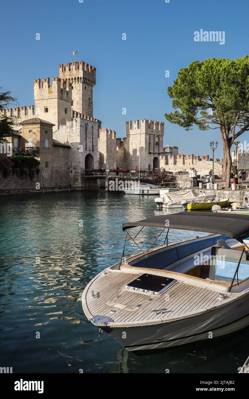 Sirmione, Italien - 25. Juni 2022: Romantischer Blick auf die Burg Scaligero mit Boot am Gardasee. Vertikale Szene des Sommertages in der Lombardei. Stockfoto