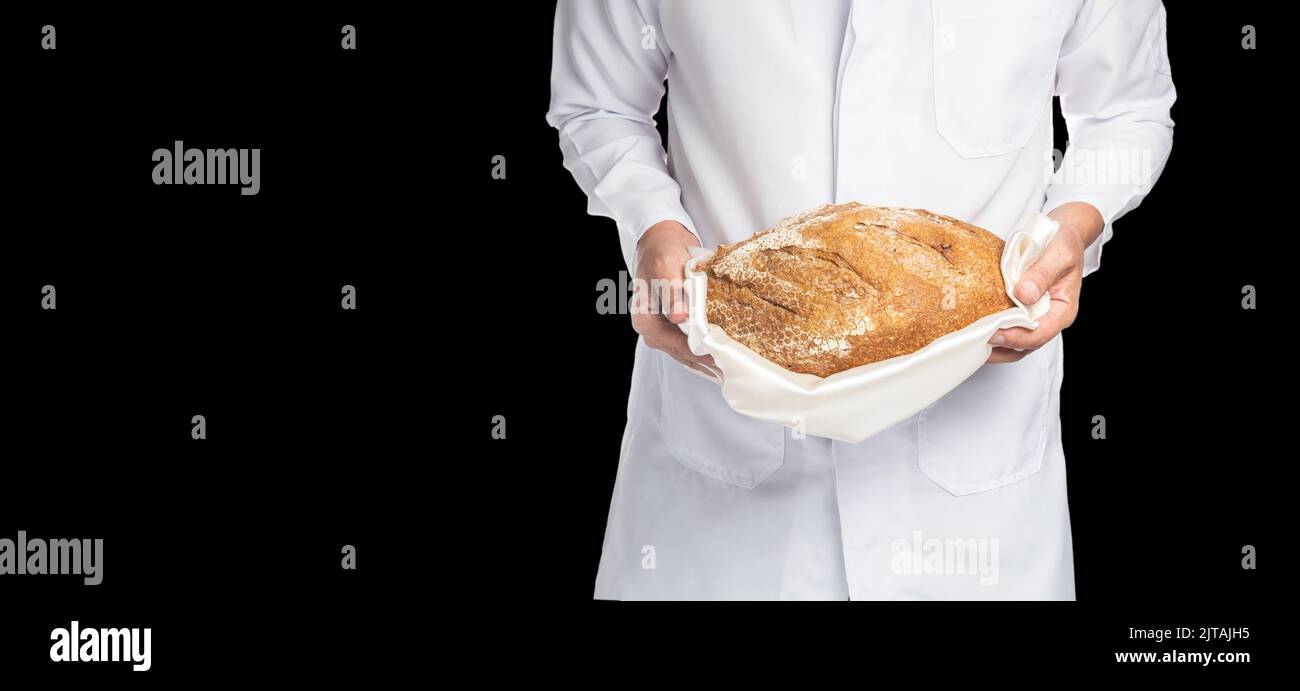 Nahaufnahme eines Bäckers in weißer Uniform mit einem Vollkornbrot in den Händen isoliert auf schwarzem Hintergrund Stockfoto