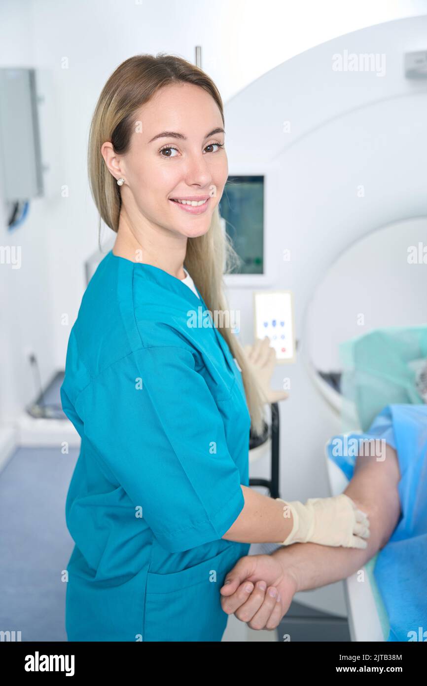 Krankenschwester in blauer medizinischer Kleidung steht in der Nähe eines lügenden Patienten Stockfoto