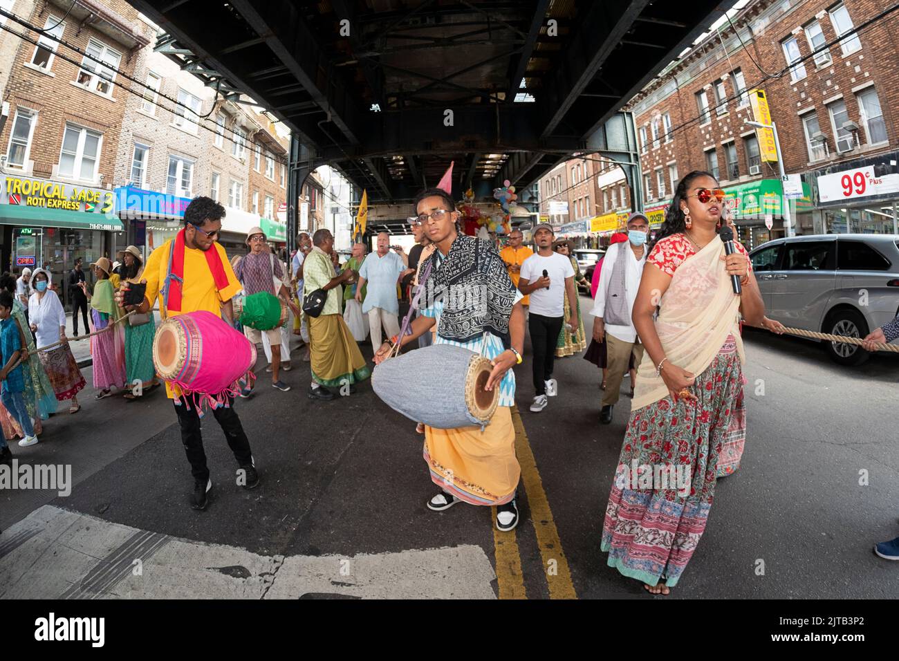 Fromme Hindu-Männer und -Frauen marschieren, singen und tanzen unter dem erhöhten A-Zug, der die Ratha Yatra 2022 in Richmond Hill, Queens, NYC, feiert Stockfoto