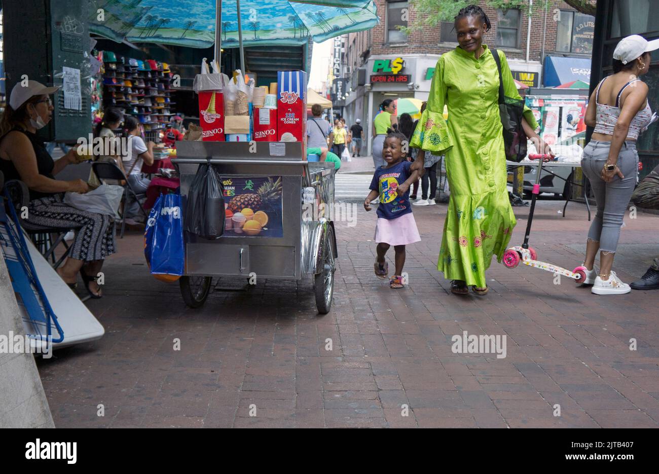 Eine Straßenszene unter dem El in Corona Queens mit einem weinenden Kind, einer Mutter, dem Kinderroller und Verkäufern. New York City, 2022. Stockfoto