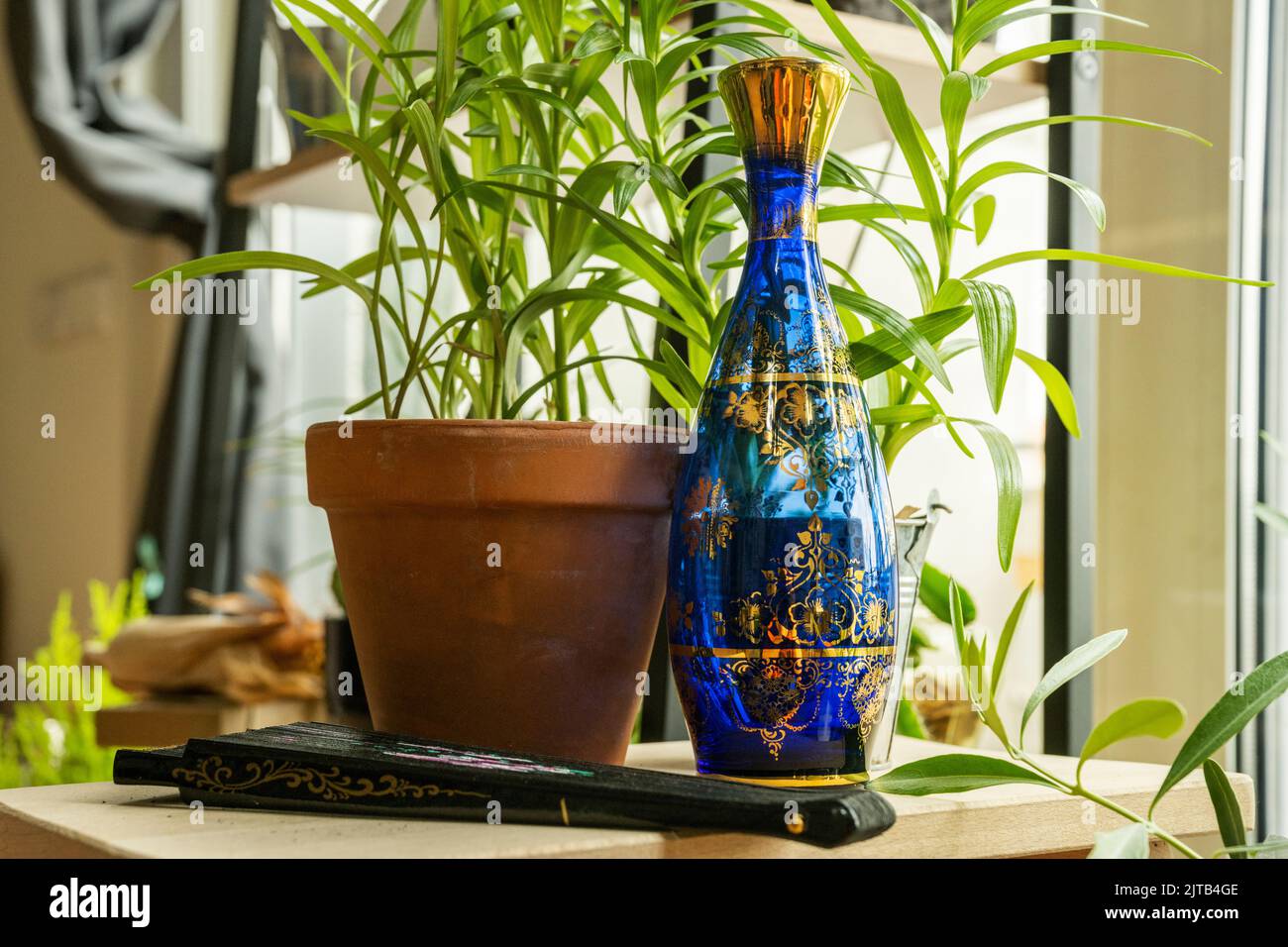 Wunderschöne blaue Glasflasche mit goldenen Zierdetails, umgeben von Töpfen und Pflanzen Stockfoto