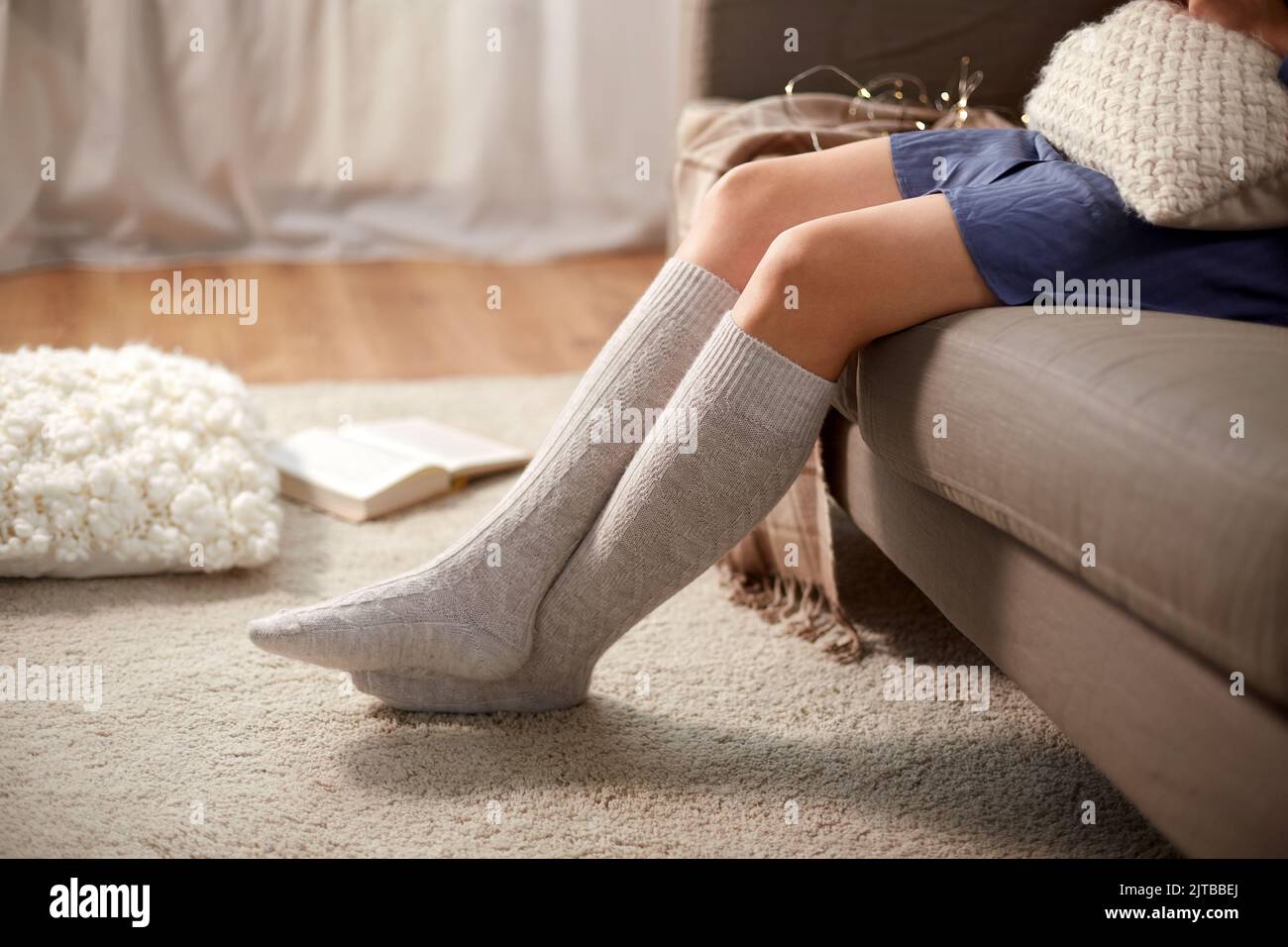 Frau in Socken mit Kissen sitzt auf dem Sofa zu Hause Stockfoto