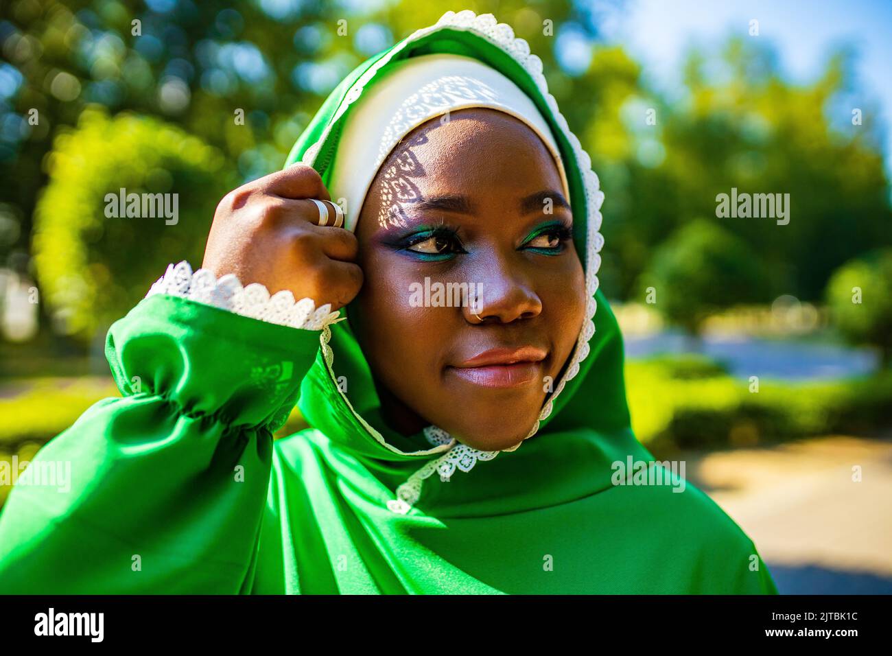 Moderne authentische multikulturelle Rasse islamische Frau in grüner Baumwolle Hijab mit wunderschönen Make-up im Freien im Sommerpark Stockfoto