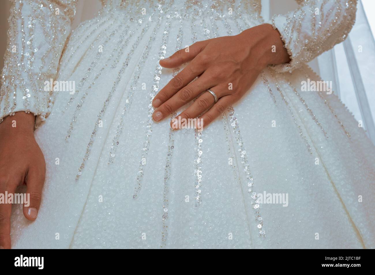 Hände auf das Kleid der Braut, Ehering mit weißem Gold am Finger der Braut, Hochzeitsdetails. Stockfoto