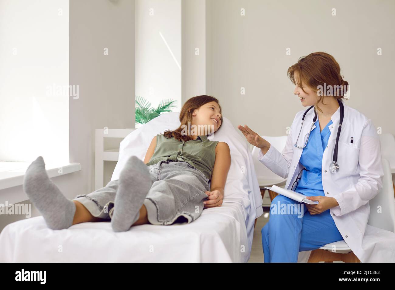 Kinderarzt im Gespräch mit einem glücklichen Teenager-Mädchen, das auf der medizinischen Untersuchungscouch liegt Stockfoto