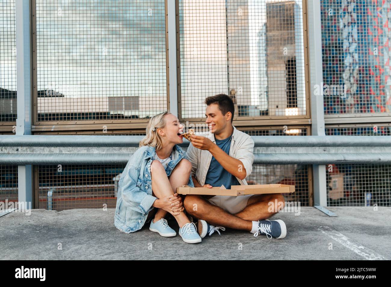 Ein glückliches Paar, das auf dem Parkplatz auf dem Dach der Stadt Pizza gegessen hat Stockfoto