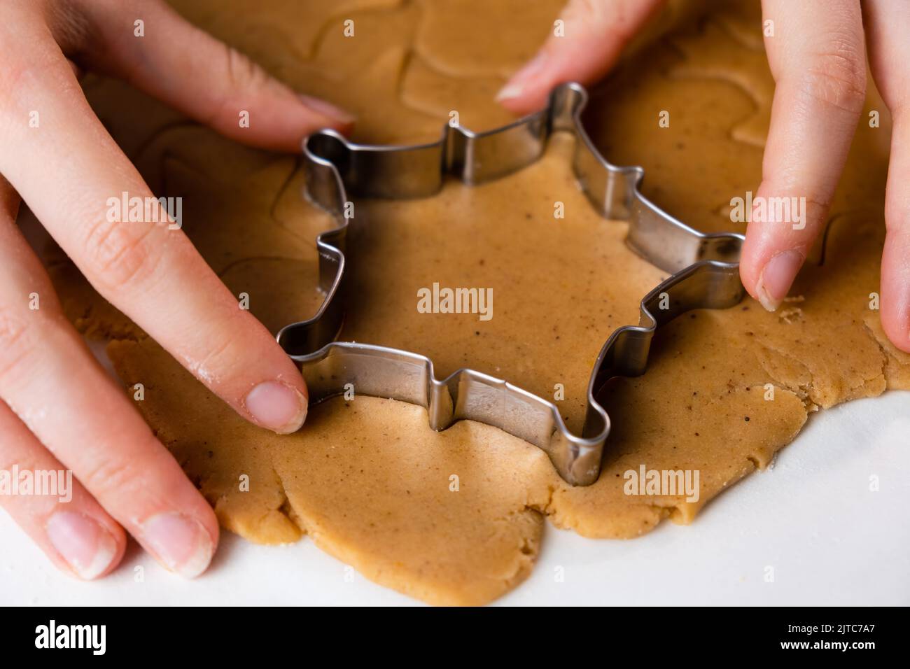 Nahaufnahme Frau Hände schneiden Cookies mit Metallform aus dem Mürbeteig. Ein Metall bildet sich in Form von Schneeflocken zur Herstellung von Lebkuchen zu Weihnachten. Stockfoto