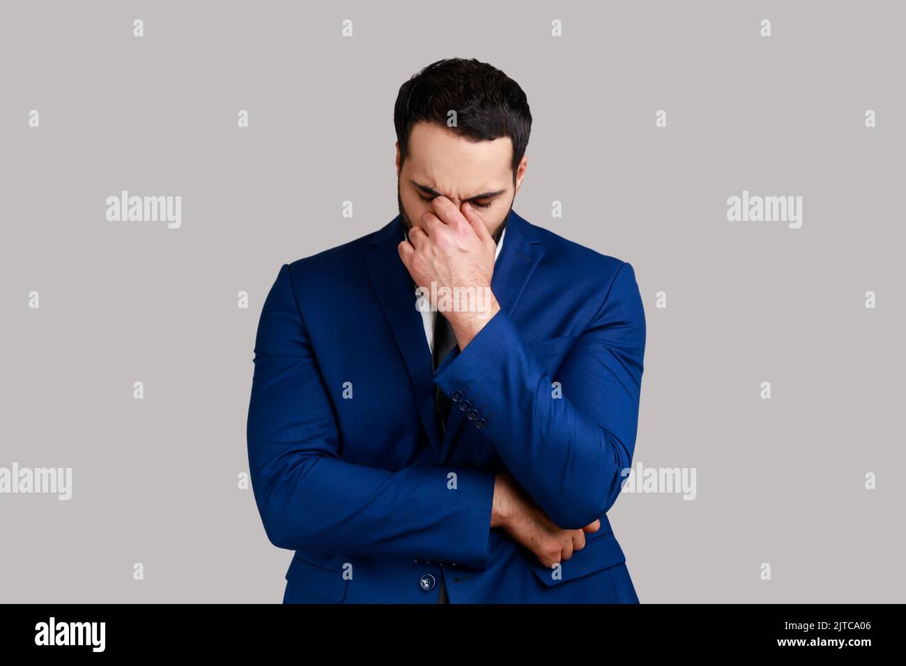 Traurig verärgert unglücklich bärtiger Geschäftsmann, der sich in der Hand versteckt und weint, sich gestresst besorgt fühlt, Trauer ausdrückt und einen offiziellen Anzug trägt. Innenaufnahme des Studios isoliert auf grauem Hintergrund. Stockfoto