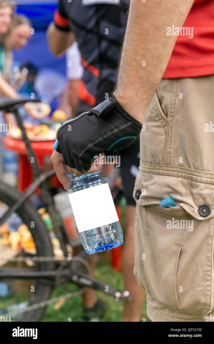 Eine Plastikflasche mit Trinkwasser mit einem sauberen Etikett in der Hand eines Radsportlers. Stockfoto