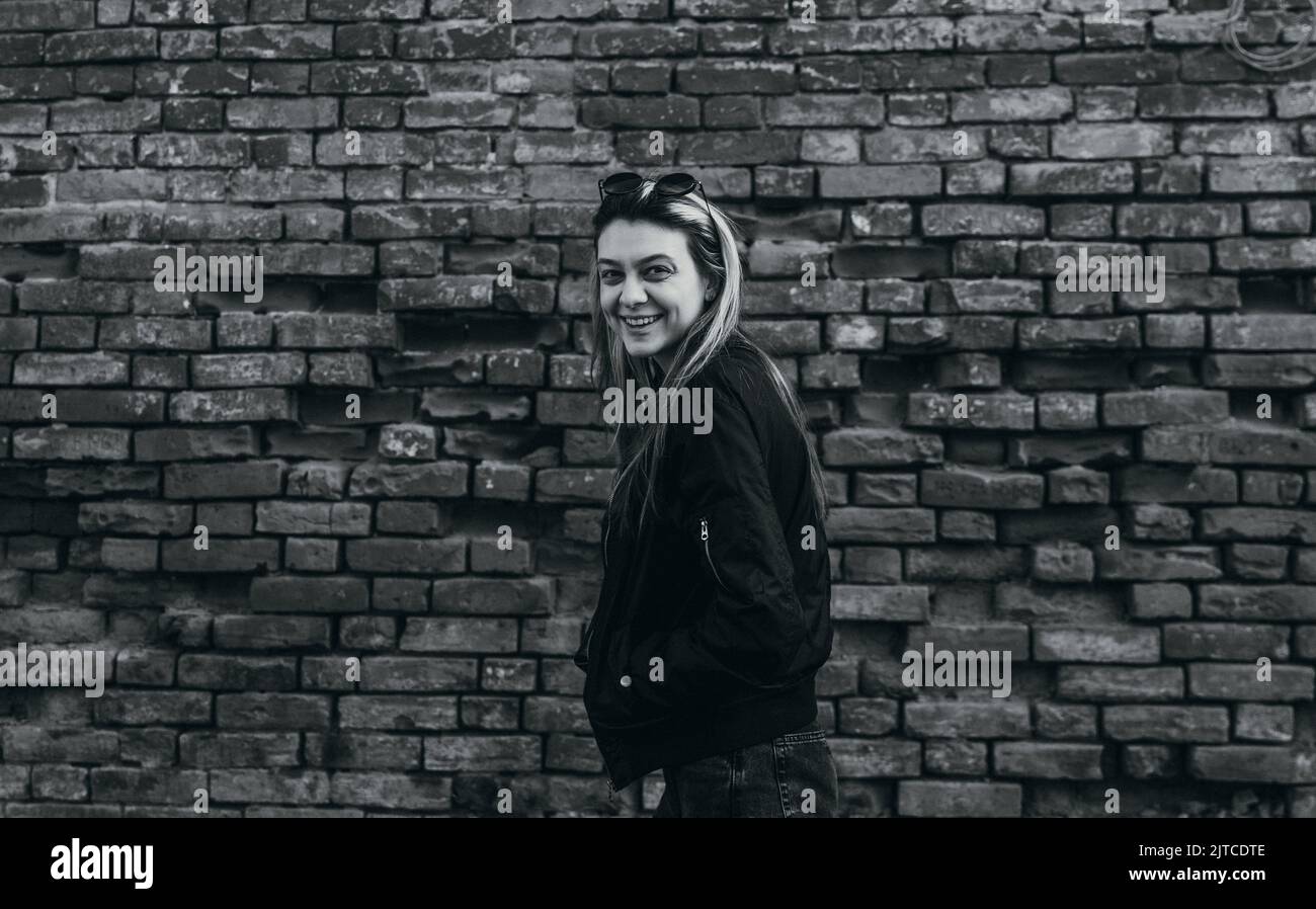 Lächelndes junges Mädchen, das auf der Straße gegen eine Backsteinmauer steht Stockfoto