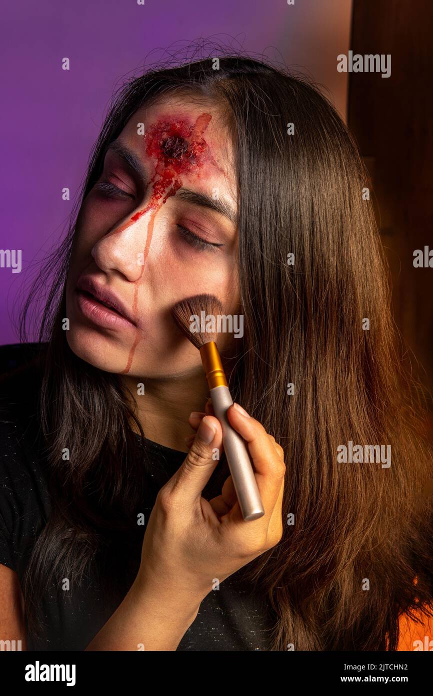 Nahaufnahme einer jungen Frau, die ein Halloween Make-up mit einem Zombie-Bild mit einer Wunde auf der Stirn anlegt Stockfoto