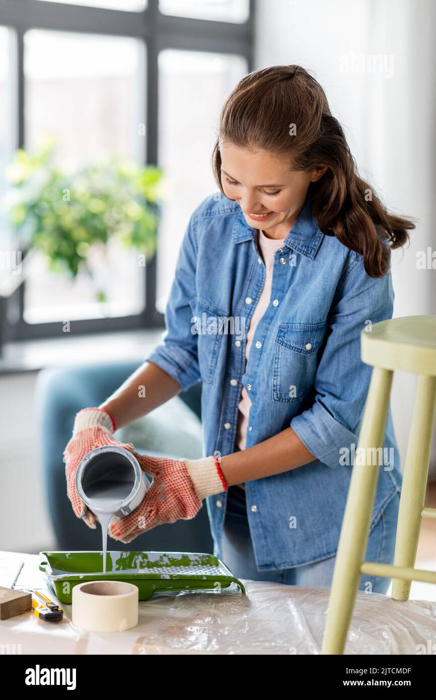 Glückliche Frau, die zu Hause graue Farbe auf das Tablett gießt Stockfoto