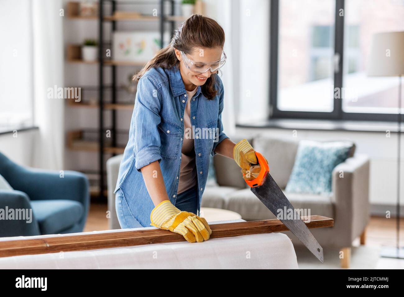 Frau mit Säge, die zu Hause Holzbrett sägt Stockfoto