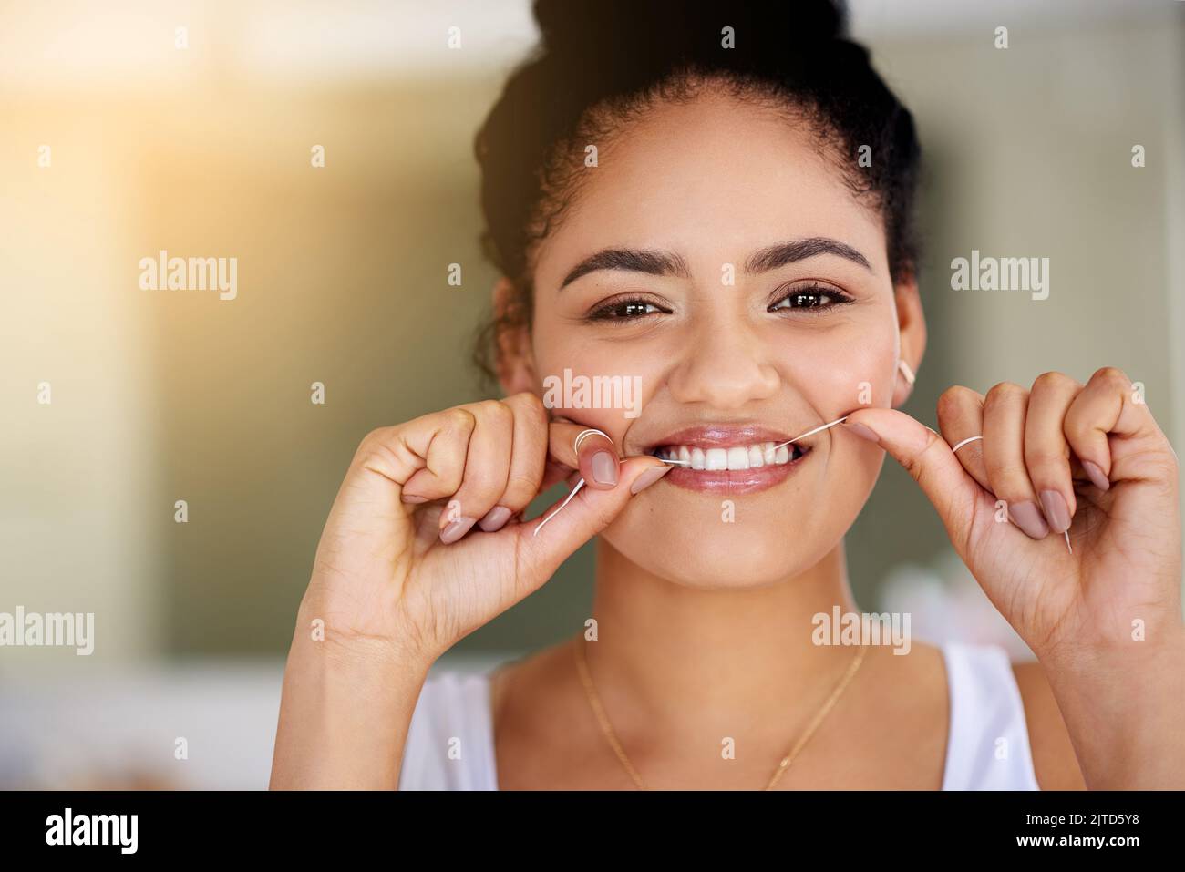 Zahnseide aus Liebe zu ihren Zähnen. Porträt einer attraktiven und glücklichen jungen Frau, die ihre Zähne mit Zahnseide putzt. Stockfoto