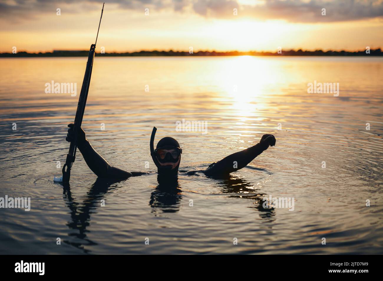 Speerfischertaucher feiern, während sie in Meerwasser getaucht sind und eine Speergun in der Hand halten. Fröhlicher Taucher, der beim Sonnenuntergang Speerfischen genießt. Stockfoto