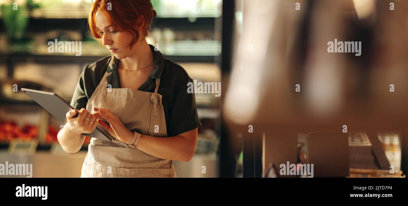 Weibliche Ladenbesitzerin, die ein digitales Tablet benutzt, während sie in ihrem Lebensmittelgeschäft steht. Erfolgreiche Unternehmerin, die ihr kleines Unternehmen mit Wireless-Techno betreibt Stockfoto