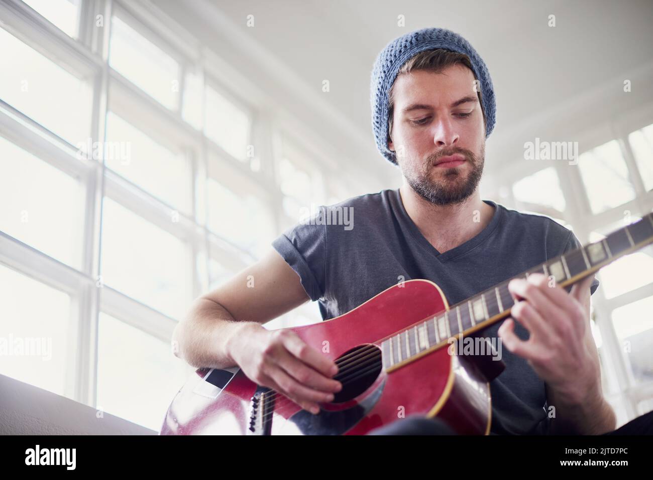 Hes ein autodidaktischer Muso. Ein hübscher junger Mann, der zu Hause Gitarre spielt. Stockfoto