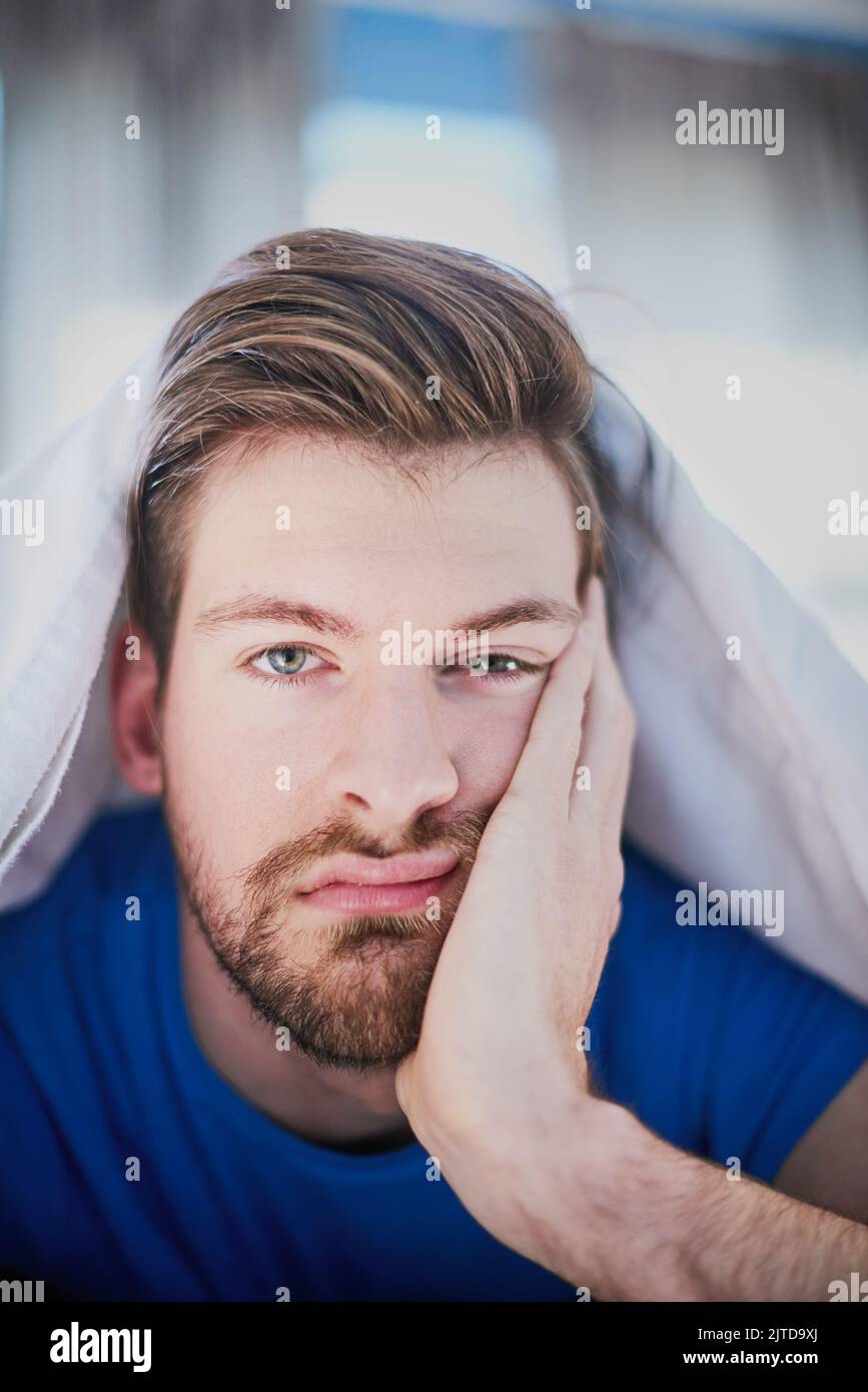 Gelangweilt und blau. Porträt eines hübschen jungen Mannes, der gelangweilt im Bett liegt. Stockfoto