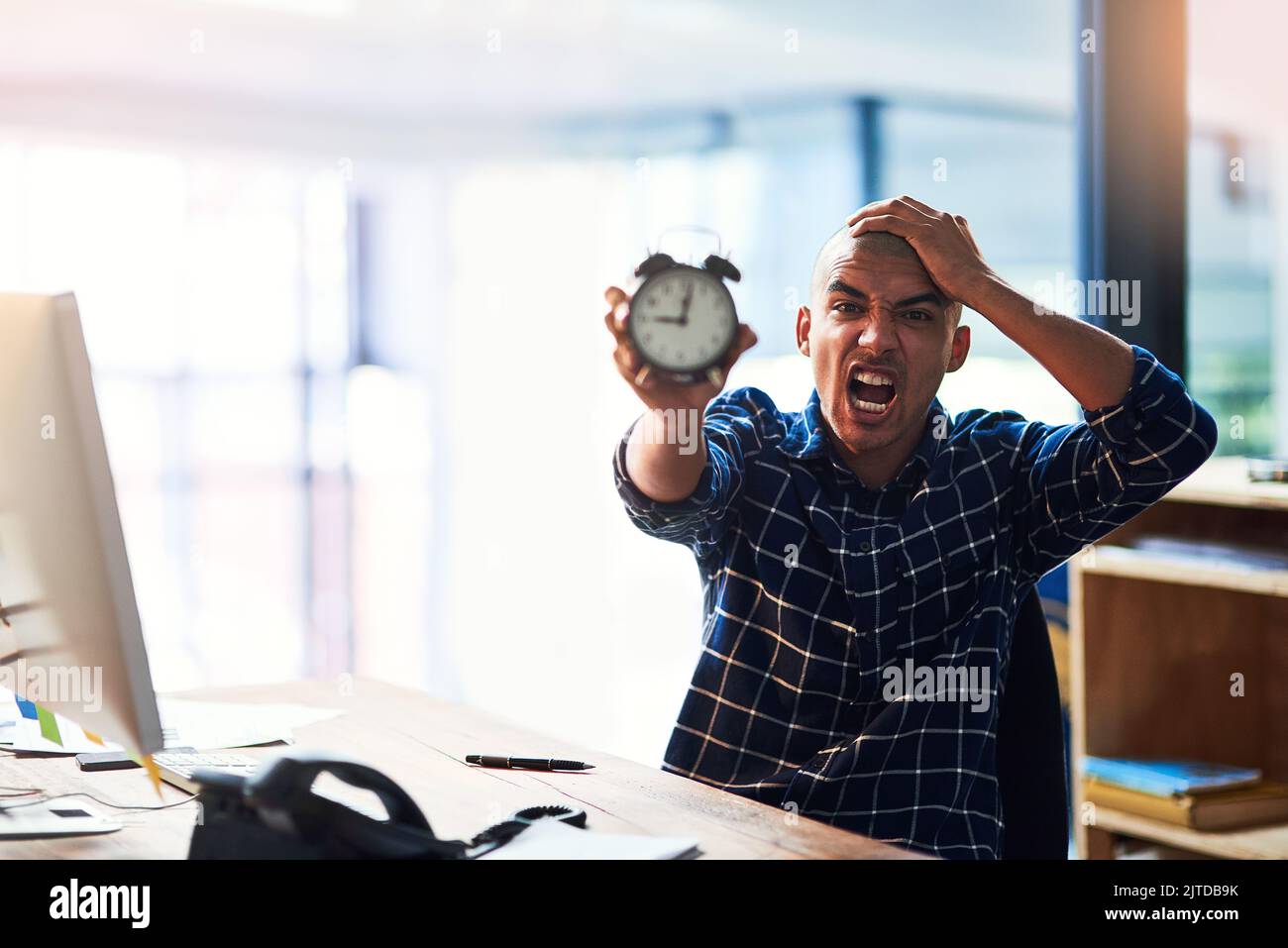 Es gibt einfach zu viel, um mit zu wenig Zeit zu tun. Porträt eines jungen Designers, der gestresst aussieht und einen Wecker hält. Stockfoto