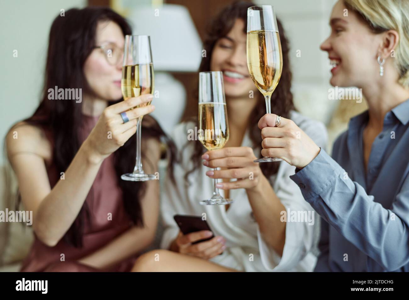Drei glückliche Mädchen mit Champagner feiern die bevorstehende Hochzeit eines von ihnen, während sie Flöten halten und auf der Junggesellinnenparty anstoßen Stockfoto