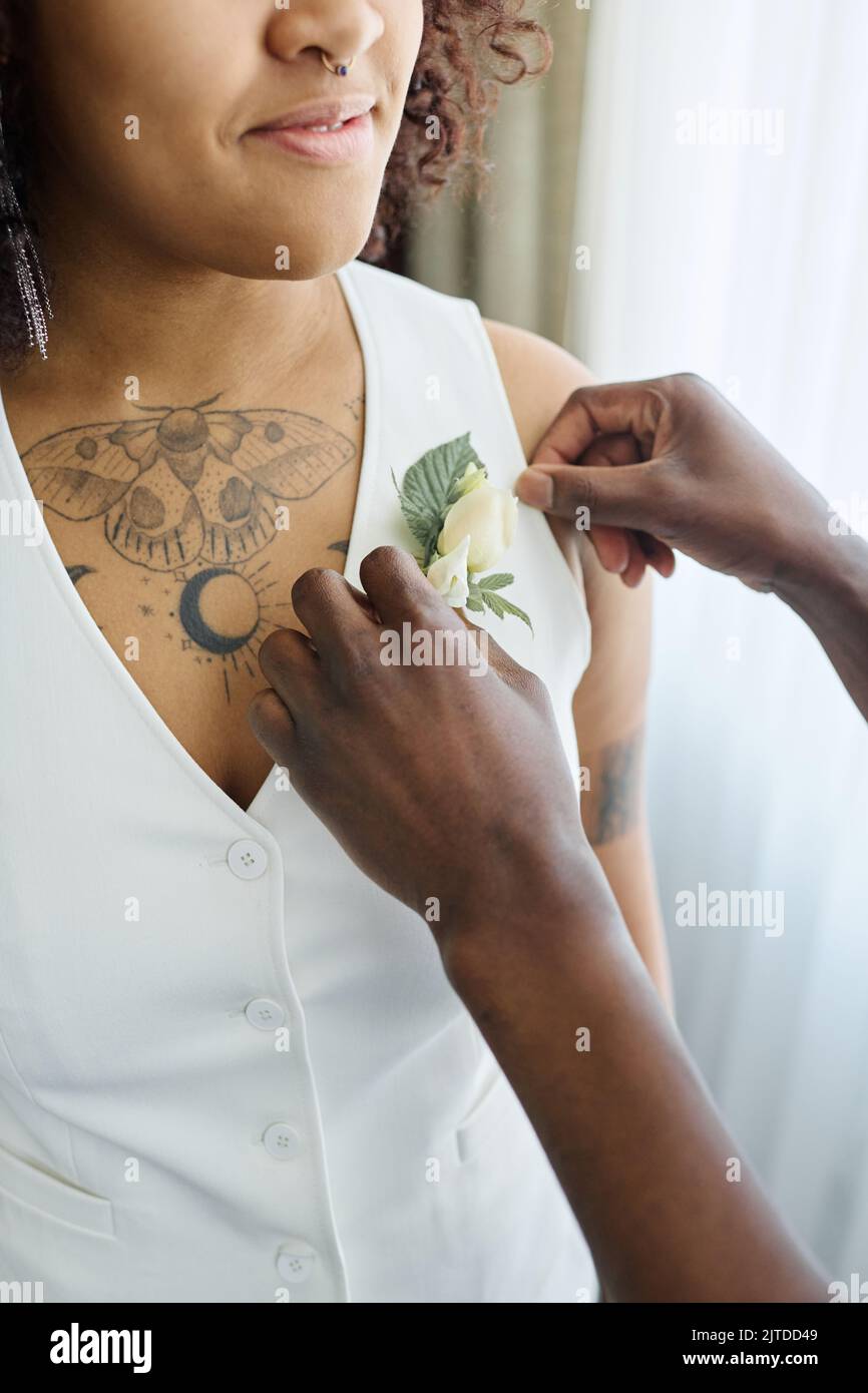 Hände eines schwarzen Mannes, der eine Knopflochblume auf die weiße elegante Weste der afroamerikanischen Braut legt, die vor ihm steht Stockfoto