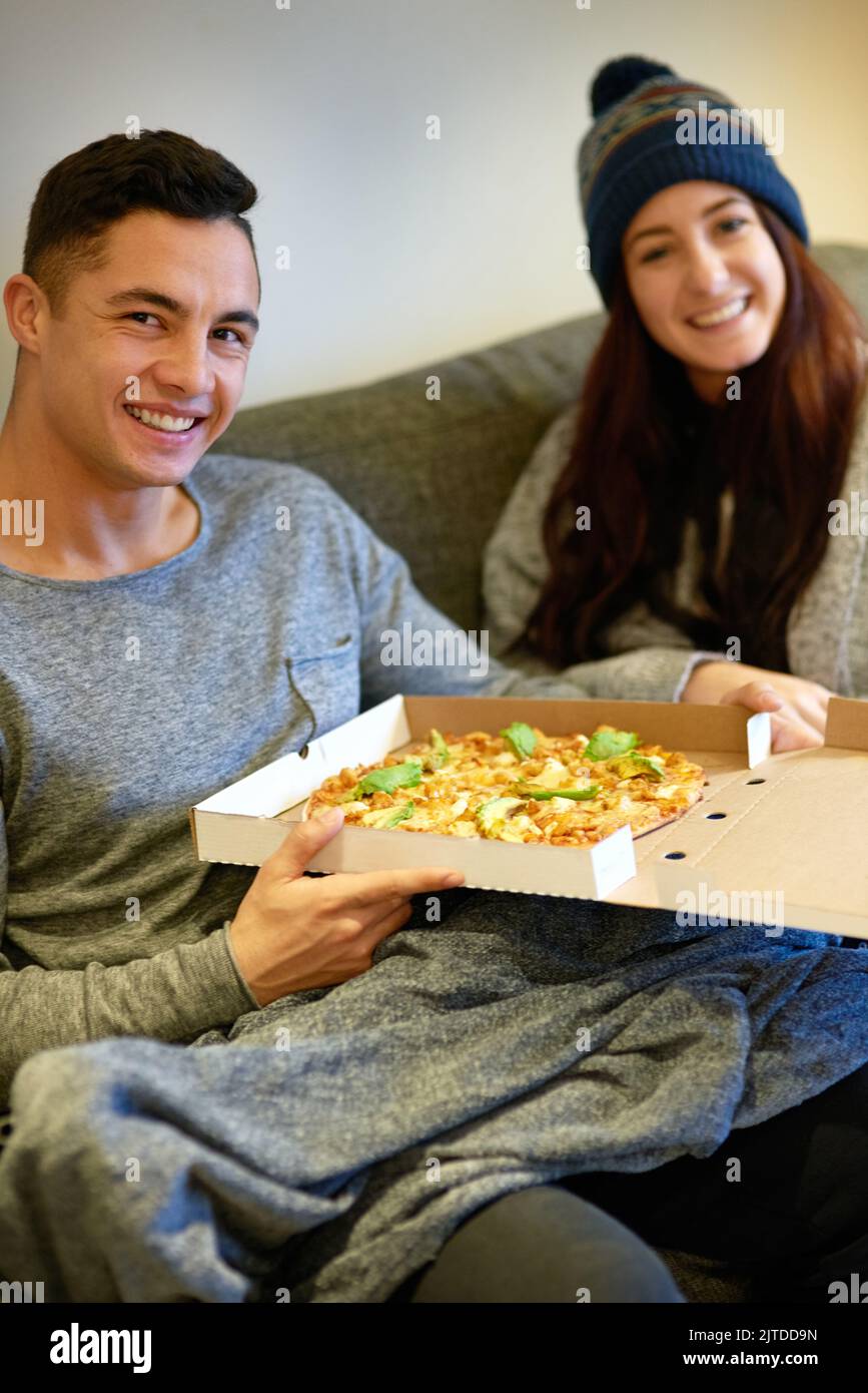Pizza ist die perfekte Kombination. Porträt eines glücklichen jungen Paares, das Pizza isst und sich zu Hause auf dem Sofa entspannt. Stockfoto
