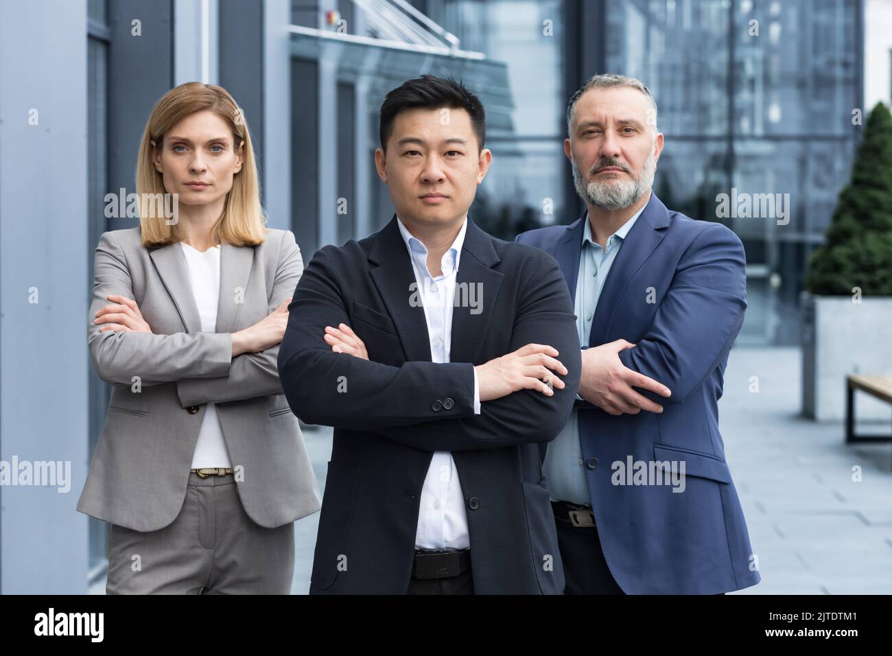 Ein erfolgreiches und seriöses Team aus drei Geschäftsleuten, Männer und Frauen, die sich mit gekreuzten Armen auf die Kamera konzentrierten, ein Porträt von Mitarbeitern außerhalb des Bürogebäudes Stockfoto