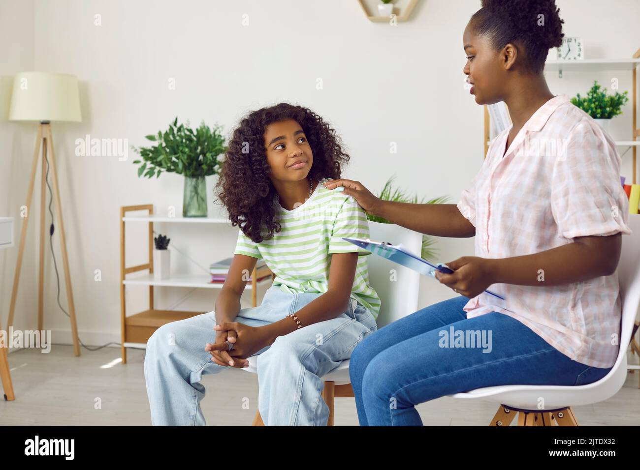 Lächelndes, dunkelhäutig gemachtes Teenager-Mädchen besucht die Therapiesitzung mit einer jungen weiblichen Kinderpsychologin. Stockfoto