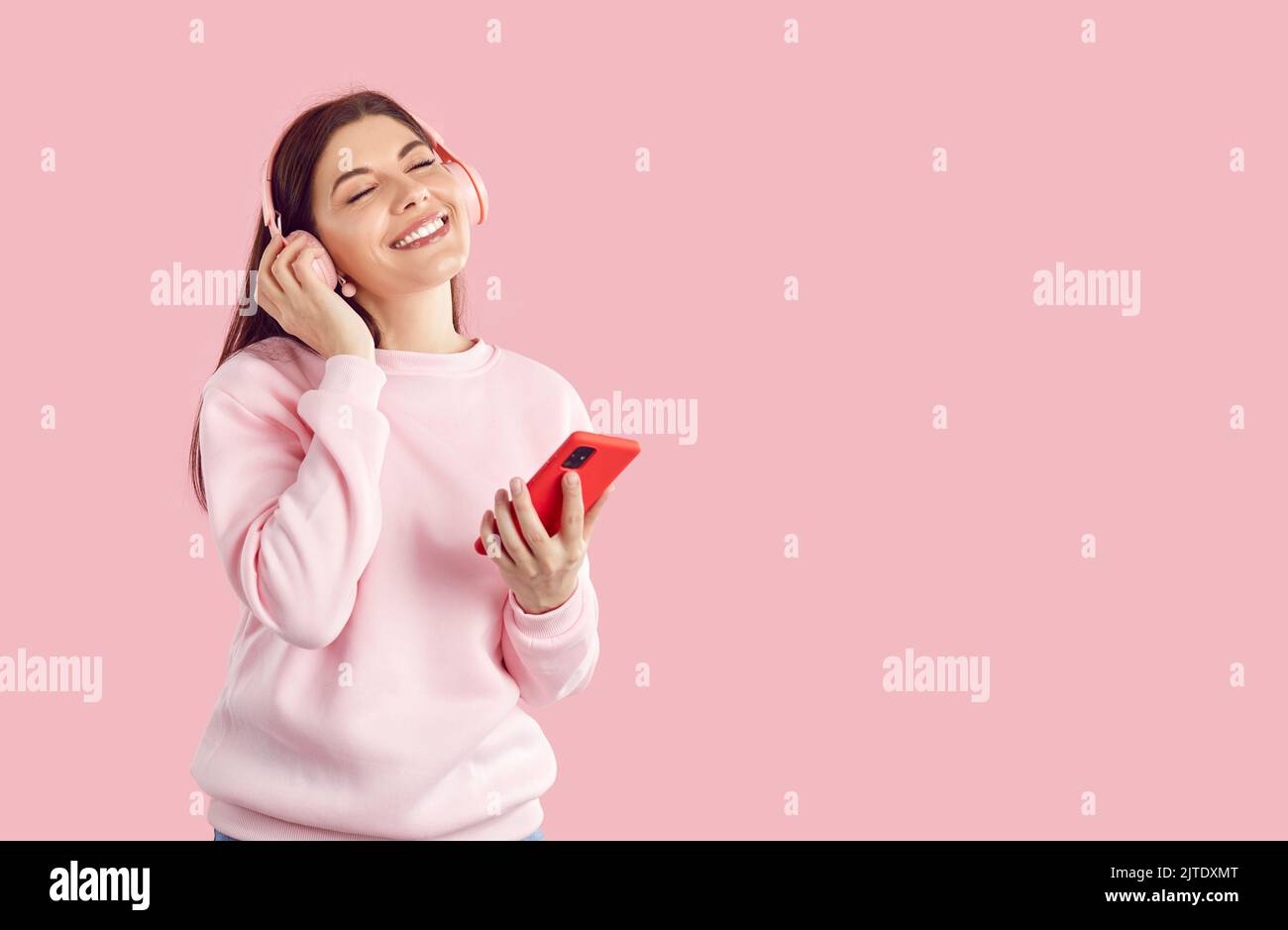 Glückliche Frau mit kabellosen Stereo-Kopfhörern und mit Mobiltelefon in der Hand genießt coole Wiedergabeliste. Stockfoto